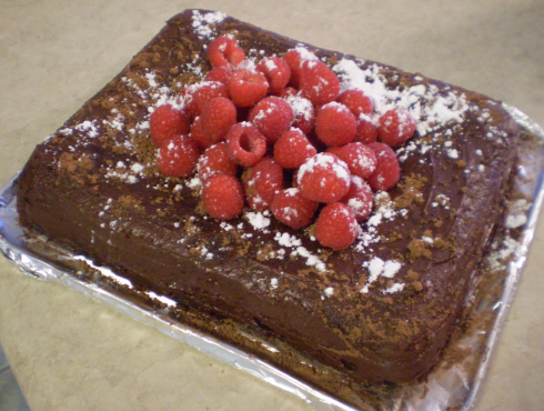 Double chocolate chip banana cake with chocolate icing and garnished with fresh raspberries, icing sugar and cocoa powder.